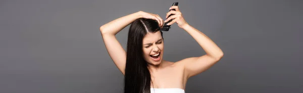 Brunette cheveux longs femme rasage tête avec rasoir électrique et crier isolé sur noir, panoramique shot — Photo de stock