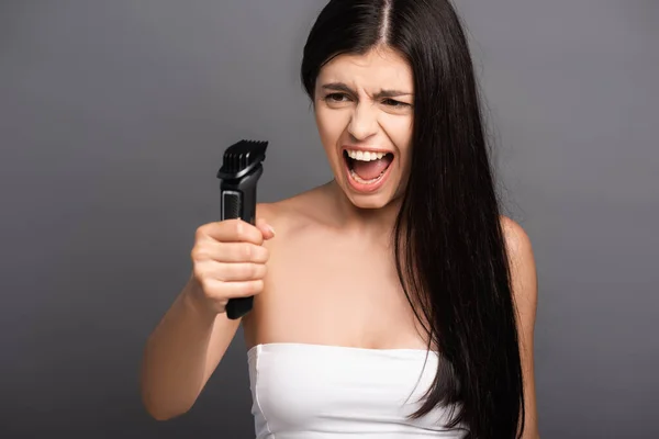 Брюнетка длинноволосая женщина, держащая электрическую бритву и кричащая изолированно на черном — стоковое фото