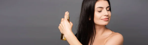 Naked brunette woman spraying oil on hair isolated on black, panoramic shot — Stock Photo