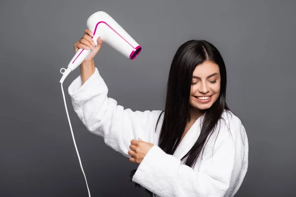 Morena de cabelos longos mulher em roupão de banho usando secador de cabelo isolado no preto — Fotografia de Stock