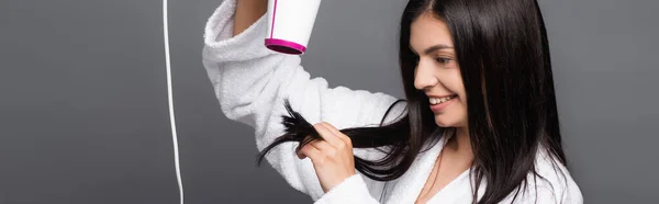 Brunette long haired woman in bathrobe using hairdryer isolated on black, panoramic shot — Stock Photo