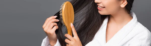 Brunette femme en peignoir brossant les cheveux et souriant isolé sur noir, panoramique shot — Photo de stock