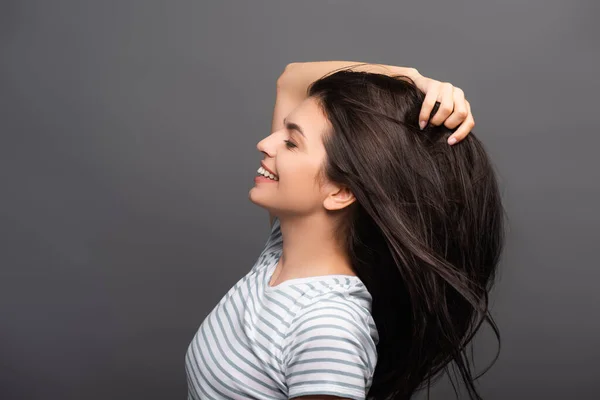 Side view of brunette woman with closed eyes smiling and touching hair isolated on black — Stock Photo