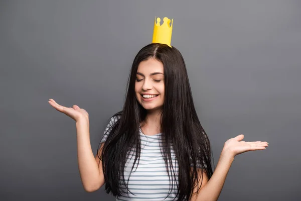 Brunette long haired woman in paper crown with closed eyes smiling isolated on black — Stock Photo