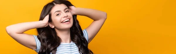 Brunette woman toughing curly long hair and smiling isolated on yellow, panoramic shot — Stock Photo