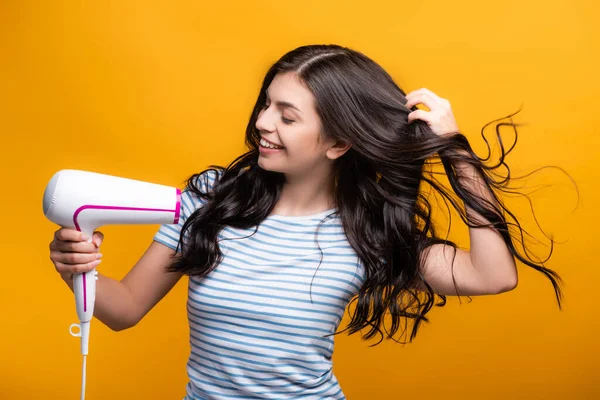 Morena mujer con rizos usando secador de pelo aislado en amarillo - foto de stock