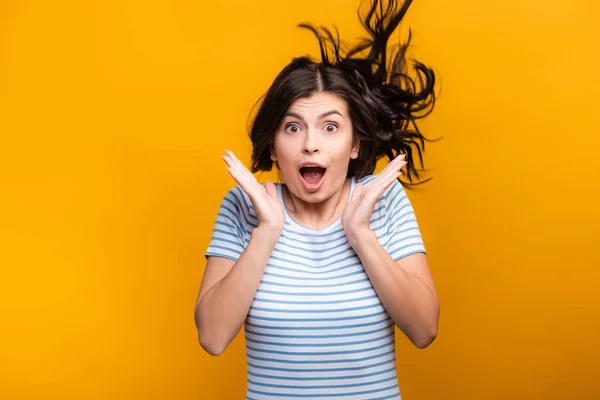 Shocked brunette long haired woman with curls jumping isolated on yellow — Stock Photo