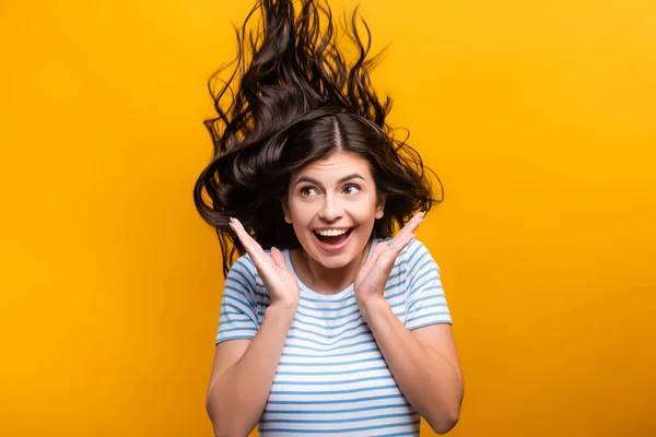 Morena mujer de pelo largo con rizos saltando y sonriendo aislado en amarillo - foto de stock