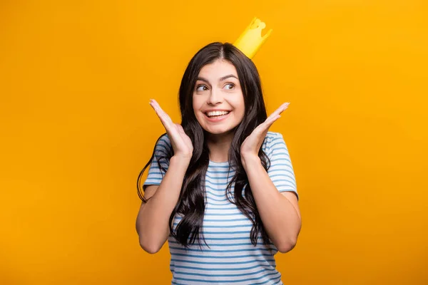 Brunette woman in paper crown smiling and looking away isolated on yellow — Stock Photo