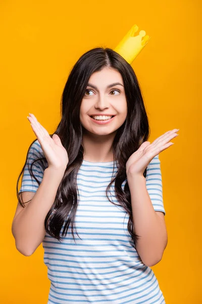 Brunette femme en papier couronne souriant et regardant loin isolé sur jaune — Photo de stock