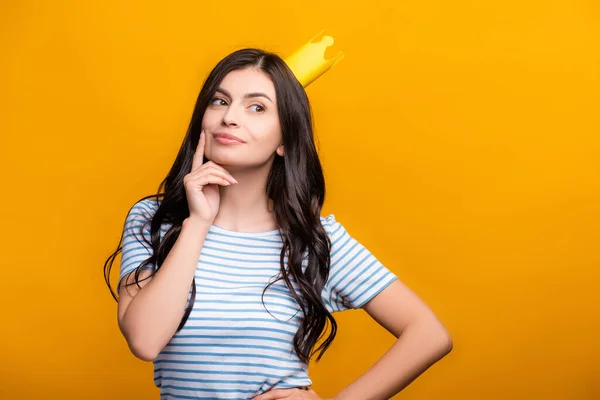 Morena pensativa en corona de papel mirando hacia otro lado aislado en amarillo - foto de stock