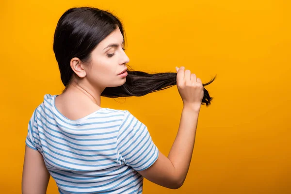 Вид ззаду брюнетка жінка тримає волосся ізольовано на жовтому — стокове фото