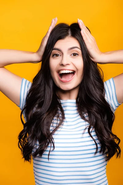 Brunette long haired woman with curls touching head and smiling isolated on yellow — Stock Photo