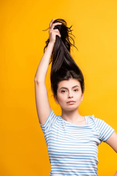 Brunette woman holding hair above head isolated on yellow — Stock Photo