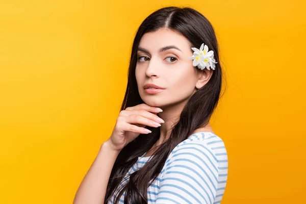 Brünette junge Frau mit Blumen im Haar, die isoliert auf gelb wegschaut — Stockfoto