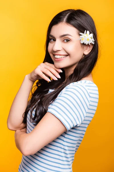 Morena joven con flores en el pelo sonriendo aislado en amarillo - foto de stock