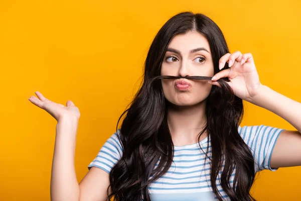 Brünette Frau mit Locken macht falschen Schnurrbart aus Haar isoliert auf gelb — Stockfoto