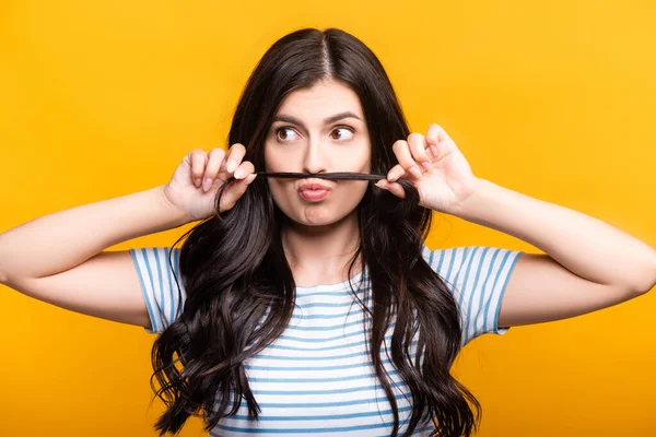 Brunette woman with curls making fake mustache from hair isolated on yellow — Stock Photo