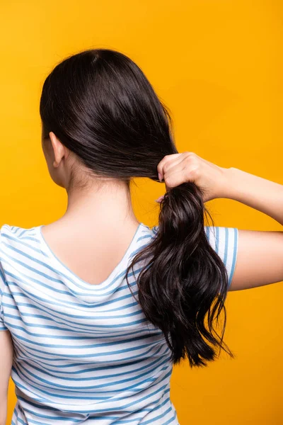 Rückansicht einer brünetten Frau mit Locken, die ihr Haar isoliert auf gelb hält — Stockfoto