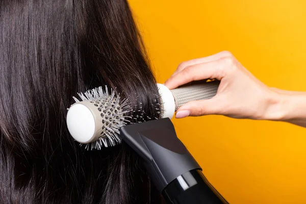 Vue recadrée du coiffeur en utilisant sèche-cheveux et brosse isolée sur jaune — Photo de stock