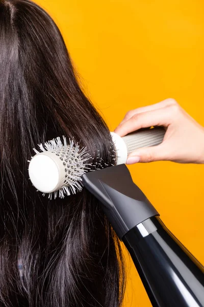 Vista ritagliata del parrucchiere utilizzando asciugacapelli e spazzola isolata sul giallo — Foto stock