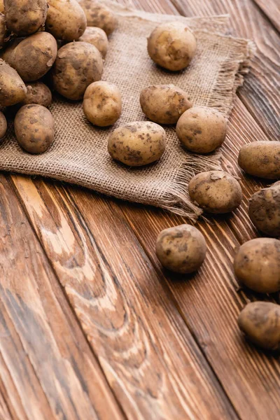 Dirty potatoes and burlap on wooden table — Stock Photo