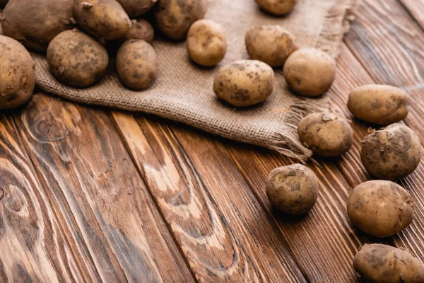 Dirty potatoes and burlap on wooden table — Stock Photo