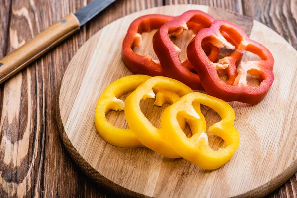 Pimientos coloridos en rodajas en tabla de cortar de madera cerca del cuchillo - foto de stock