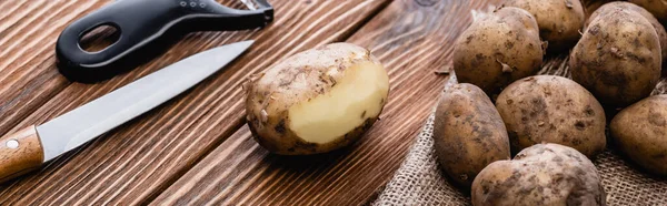 Patate sporche su tavolo in legno con pelapatate e coltello, colpo panoramico — Foto stock