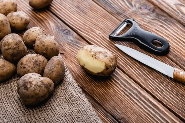 Schmutzige Kartoffeln auf Holztisch mit Schäler und Messer — Stockfoto