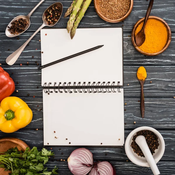 Vue de dessus des légumes et des épices colorées fraîches près du bloc-notes vierge sur la surface en bois — Photo de stock