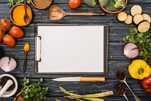 Vista superior de verduras y especias coloridas frescas cerca del portapapeles en blanco en la superficie de madera - foto de stock