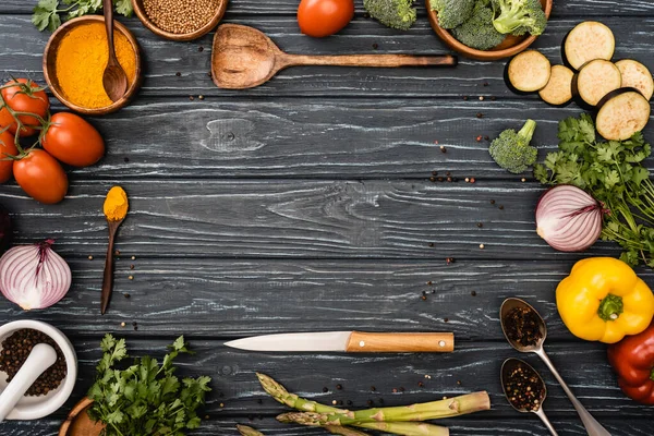 Vista superior de verduras frescas de colores, especias cerca de cuchillo y espátula en la superficie de madera - foto de stock