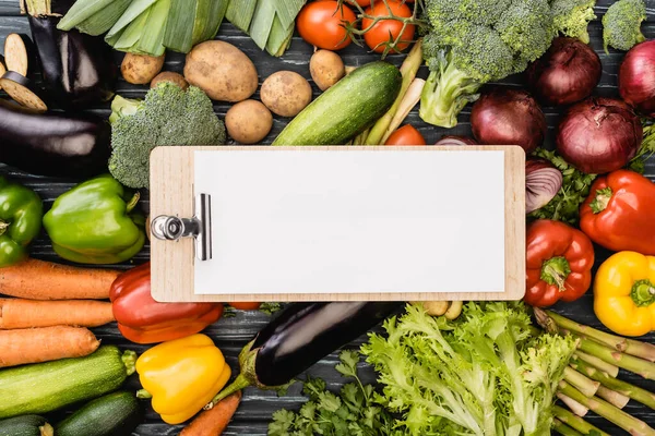 Vista superior de verduras frescas de colores alrededor del portapapeles vacío con papel — Stock Photo