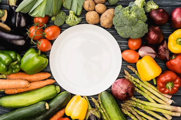 Вид зверху на свіжі барвисті овочі навколо порожньої тарілки — стокове фото