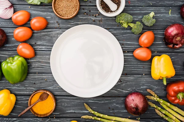 Top view of fresh colorful vegetables and spices near empty plate on wooden surface — Stock Photo