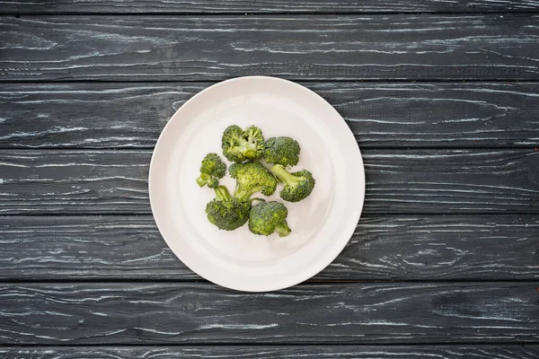 Top view of fresh broccoli on plate on wooden surface — Stock Photo