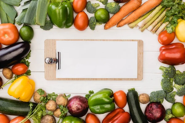 Draufsicht auf frisches reifes Gemüse und Obst in der Nähe leeres Klemmbrett auf weißem Holzgrund — Stockfoto