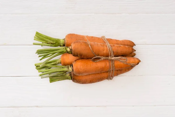 Vue du dessus des carottes attachées à la corde sur une table en bois blanc — Photo de stock