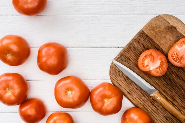 Vista superior de tomates maduros sobre tabla de cortar con cuchillo sobre mesa de madera blanca - foto de stock