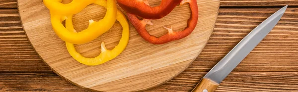 Vista dall'alto di colorati peperoni affettati sul tagliere di legno vicino al coltello, colpo panoramico — Foto stock