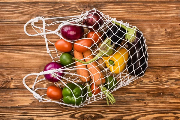 Top view of fresh ripe vegetables in string bag on wooden table — Stock Photo