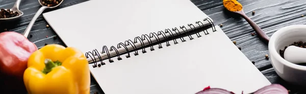 Selective focus of fresh colorful vegetables and spices near blank notebook on wooden surface, panoramic shot — Stock Photo