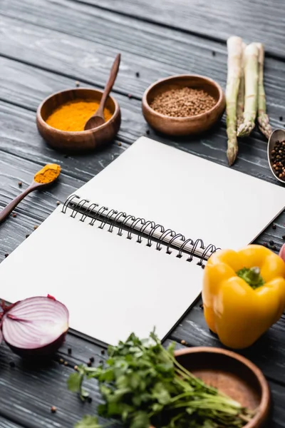 Selective focus of fresh colorful vegetables and spices near blank notebook on wooden surface — Stock Photo