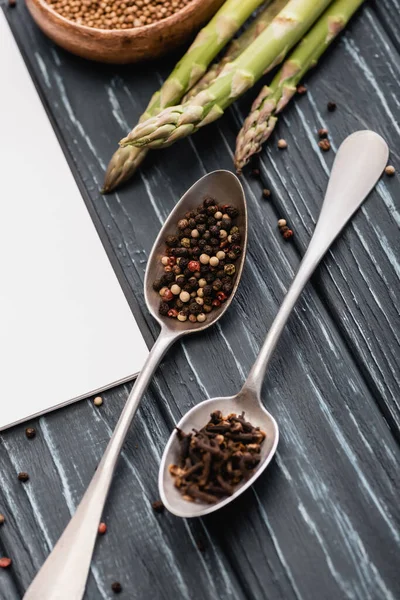 Spices in spoons near asparagus on wooden surface — Stock Photo