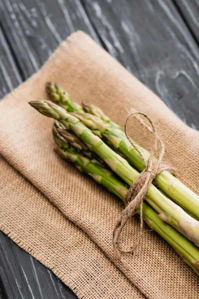 Fresh green asparagus on burlap on wooden surface — Stock Photo