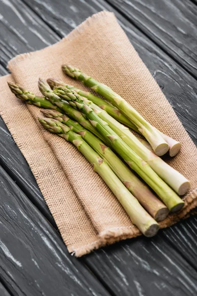 Fresh green asparagus on burlap on wooden surface — Stock Photo