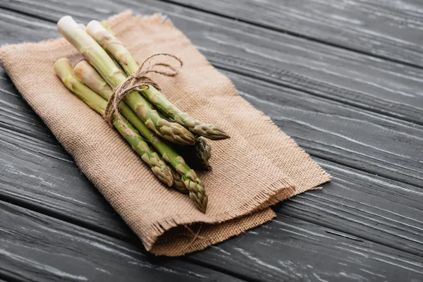 Bundle of fresh green asparagus on burlap on wooden surface — Stock Photo