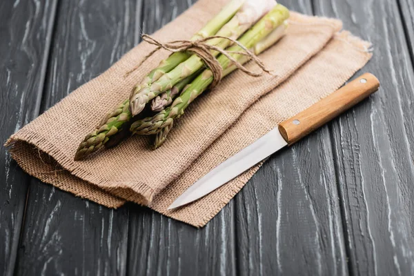 Fresh green asparagus on burlap with knife on wooden surface — Stock Photo