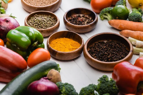 Selective focus of fresh ripe vegetables and fruits around bowls with spices on wooden white background — Stock Photo